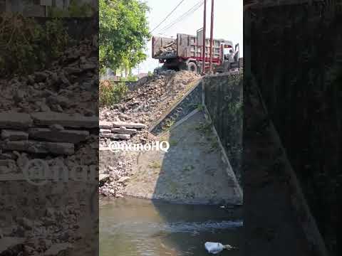 dumper truck unloading debris from asphalt road on a riverside