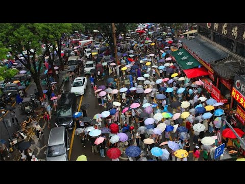 游客雨中逛西安小南门早市，撑着伞排长队吃西安小吃，伞阵真壮观