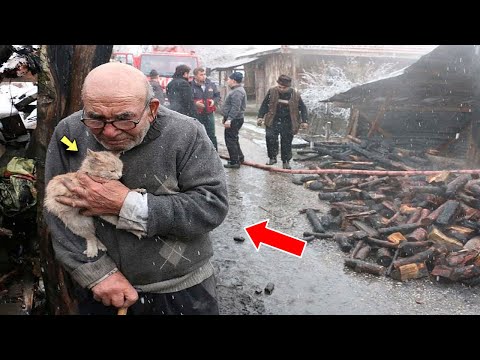 An old man tearfully hugs a cat as fire destroys his house.